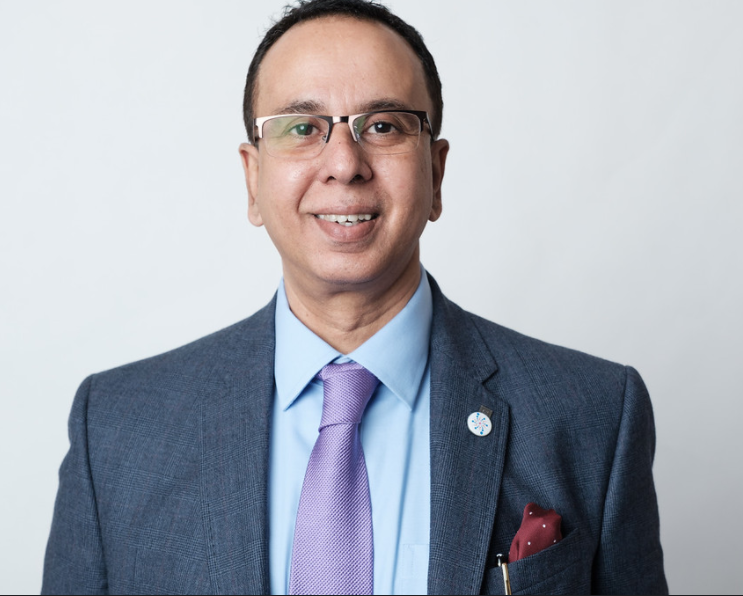 A professional man wearing glasses and a suit, smiling against a plain background.